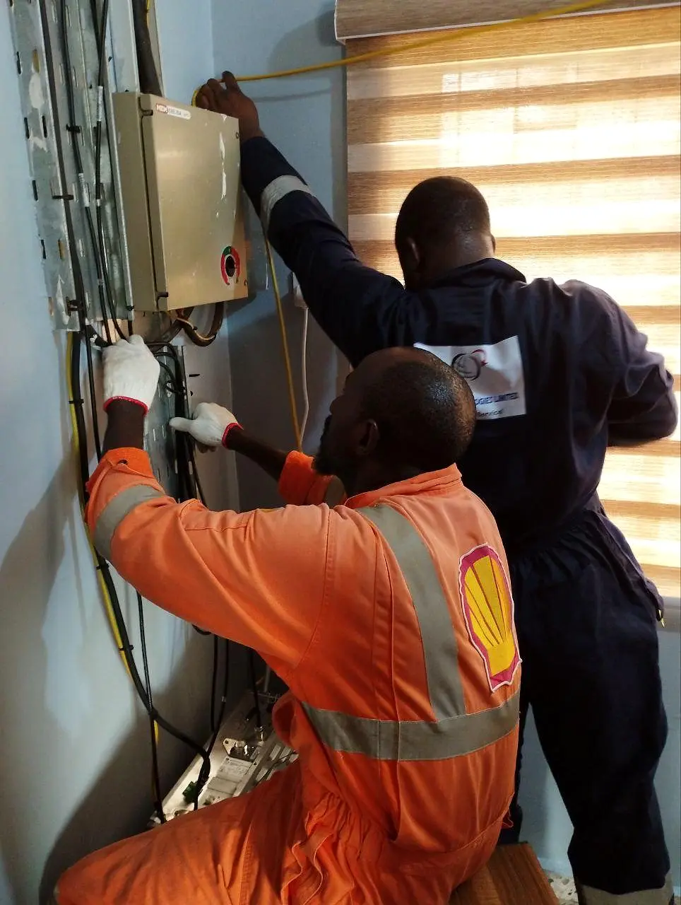 Two technicians routing and terminating communications cabling at a flow-station equipment cabinet